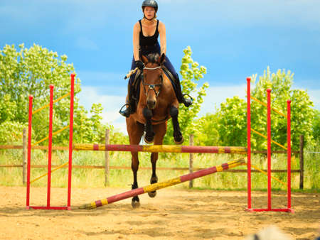 Taking care of animals, horsemanship, western competitions concept. Jockey young girl doing horse jumping through hurdle on sunny dayの写真素材