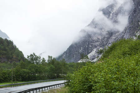 Road winding through norwegian mountains. Beautiful green summer landscape on foggy rainy day. Travel and tourism.の写真素材