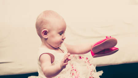 Lesson of walking. Sweet adorable baby girl thinking about make step. Little child toddler wearing princess dress with red small shoes.の写真素材