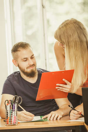 Teaching Concept. Female young teacher or tutor with male student in classroom with papers, laptop computer. Studies course teamworkの写真素材