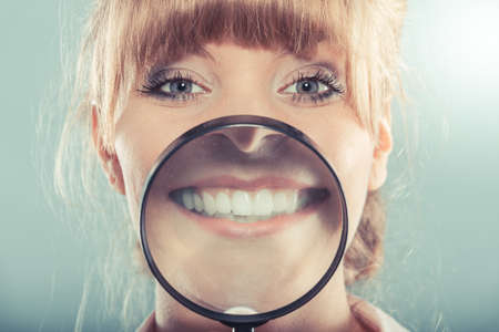 Happy young woman showing white teeth through magnifying glass.の写真素材