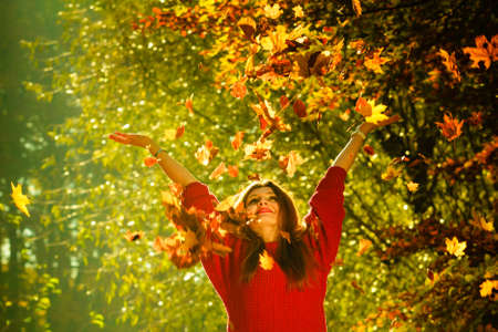 Woman playing with autumnal leaves. Young girl in park tossing foliage. Nature outdoor relax scenery concept.の写真素材