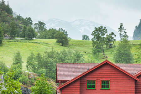 Wooden cottage cabin in the valley. Green summer misty mountains in the background. Foggy rainy weather. Norway.の写真素材
