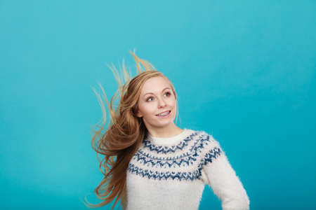 Hairstyles ideas, happiness concept. Crazy teenage woman wearing winter jumper with windblown blonde hairの写真素材