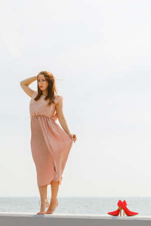 Hobby, idyllic aspects of femininity concept. Woman walking on jetty without shoes wearing beautiful long light pink dress.の写真素材