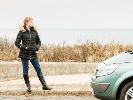 Auto traveling concept. Blonde driver woman in winter clothes standing next to her car.の写真素材