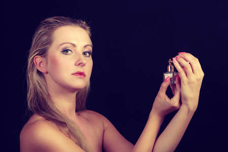 Smell, elegance concept. Beautiful elegant blonde woman with necklace holding and applying perfume...