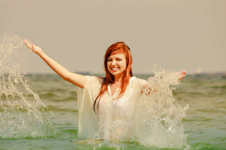 Summer fun, recreation outside concept. Redhead adult woman playing in water during summertime, having great time and smiling joyfullyの写真素材
