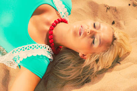 Holidays relax time concept. Blonde woman lying on sand. Lady has big necklace. Female is chilling on the beach.の写真素材