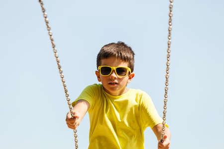 Rest and relax for children. Little boy in sunglasses resting swinging outdoor. Adorable child having fun playing in playground.の写真素材