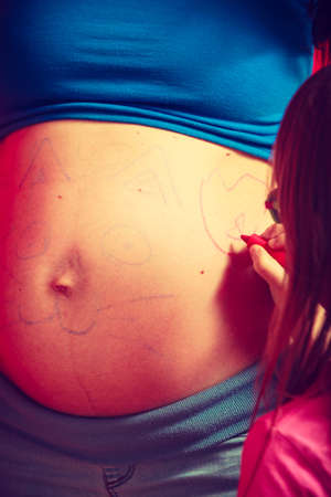 Childhood, family love concept. Toddler girl drawing on her mother big pregnant bellyの写真素材