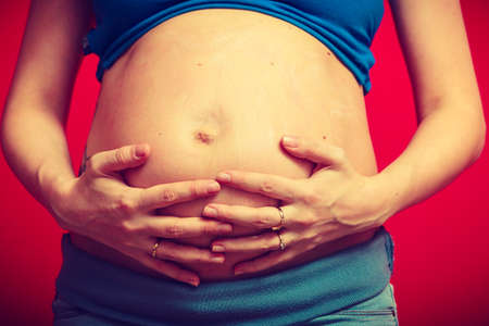 Parenthood, waiting for baby concept. Adult woman showing her big pregnant belly. Indoor shot on red backgroundの写真素材