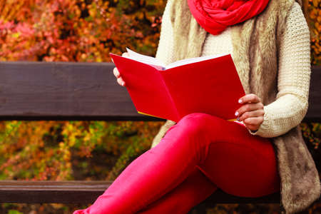 Woman fashion girl relaxing in autumnal park reading book sitting on bench. Fall lifestyle concept.の写真素材