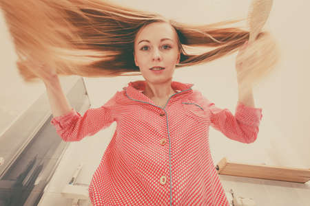 Woman wearing pajamas in bathroom having fun while brushing her long blonde hair, windblown hairdo, shot from bottom.の写真素材