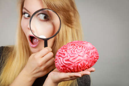 Blonde woman holding magnifying glass investigating something and looking closely at fake brain.の写真素材