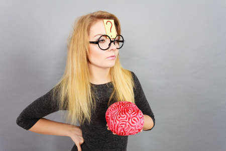 Weird blonde woman holding brain having something on mind, thinking of idea.の写真素材
