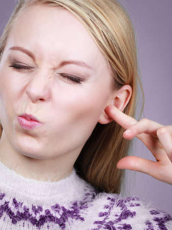 Hearing problems concept. Young blonde woman covering ears with her fingers making funny face.