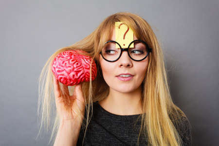 Weird blonde woman holding brain having something on mind, thinking of idea.の写真素材