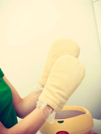 Handcare, beauty studio wellness treatments concept. Woman getting paraffin hand treatment at spa salon wearing big gloves.の写真素材