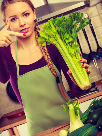Woman in kitchen holding green fresh stemmed celery. Young housewife cooking. Healthy eating, vegetarian food, dieting and people concept.の写真素材