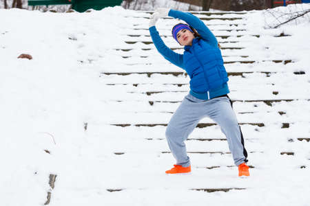 Outdoor sport exercises, sporty outfit ideas. Woman wearing warm sportswear training exercising stretching arms outside during winter.の写真素材
