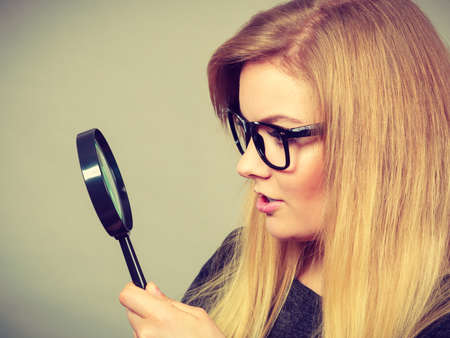Blonde woman holding magnifying glass investigating something and looking closely, trying to find solution.の写真素材