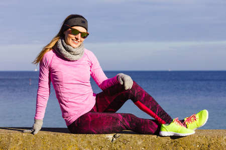 Woman resting relaxing after doing sports outdoors. Fitness girl female jogger wearing warm sporty clothes in cold day weather on seaside taking breakの写真素材