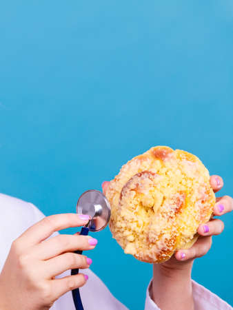 dietitian nutritionist checking examine sweet roll bun with stethoscope. Woman with fattening junk food. Bad unhealthy eating nutrition concept. Copy space for textの写真素材