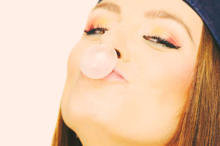 Fun entertainment with bubble. Funky girl making balloon. Lady with chewing gum. Wearing navy cap. Female has colourful make up.の写真素材