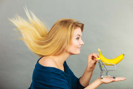 Buying healthy food, vegetarian, gluten free, vegan products. Happy woman with windblown hair holding shopping cart with banana insideの写真素材