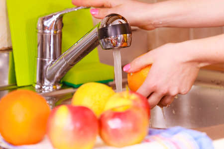 Woman young housewife washing fresh orange fruits in kitchen under water stream, preparation salad vegetarian meal. Healthy eating, cooking, dieting and people conceptの写真素材
