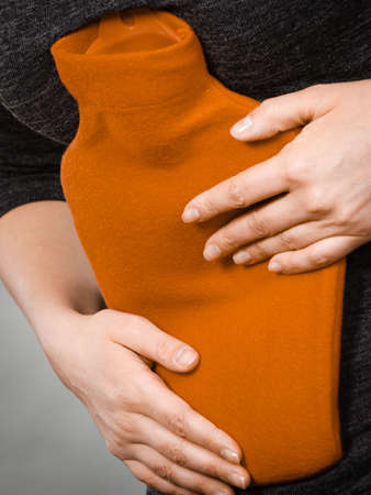 Painful periods and menstrual cramp problems concept. Woman having stomach cramps feeling very unwell holding hot water bottle.の写真素材