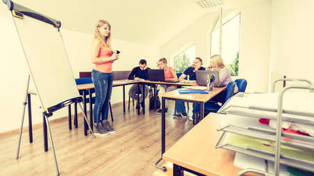 Young teacher near whiteboard teaching to bored college students in classroom