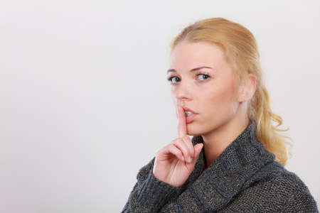 Gestures, symbols of quiet concept. Portrait, blonde adult woman holding finger close to lips...