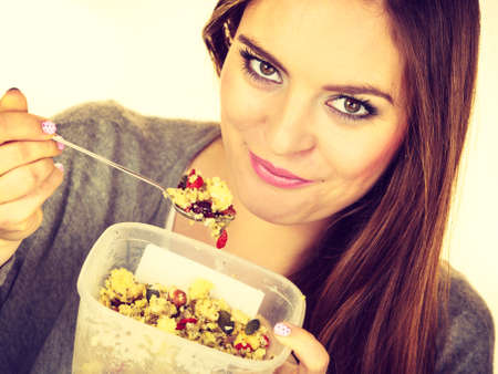 Woman eating oatmeal with nuts and dried fruits for breakfast. Girl holds plastic container take homemade lunch with healthy eating. Dieting nutrition conceptの写真素材