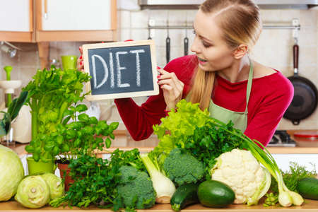 Young woman in kitchen having many green vegetables presenting board with diet sign.の写真素材