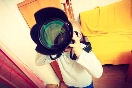 Child passion and hobbies concept. Kid playing with big professional digital camera, photographing various things in houseの写真素材
