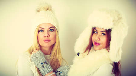 Clothing people fashion concept. Two ladies in winter outfit. Blonde woman together with mulatto girl, wearing white warm clothes.の写真素材
