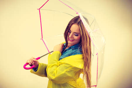 Woman rainy smiling girl wearing waterproof yellow coat standing under umbrella having fun. Meteorology, forecasting and weather season conceptの写真素材