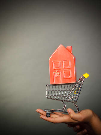 Buying property or home, real estate investment concept. Woman hand holding shopping cart with house insideの写真素材