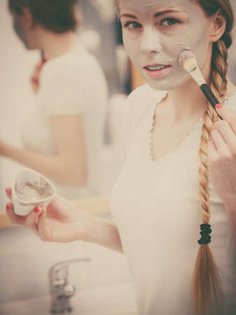 Facial dry skin and body care, complexion treatment at home concept. Happy young woman applying grey mud mask on her face with brush.の写真素材