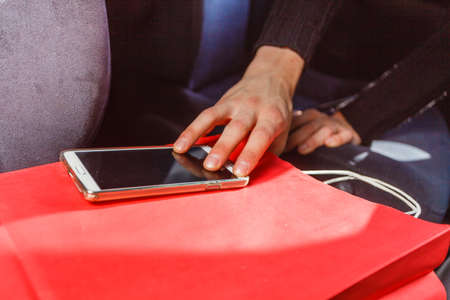 Anti theft system problem concept. Burglar thief man wearing black clothes breaking into car, stealing smartphone and red shopping bagの写真素材