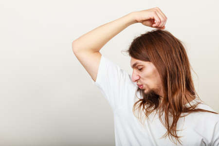 Expression of very bad smell. Young long haired sweaty man making hand gesture. Sweating concept.の写真素材