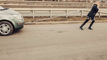 Auto assistance and insurance, troubles while traveling concept. Woman pulling broken car on roadの写真素材