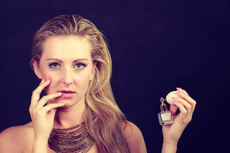 Smell, elegance concept. Beautiful elegant blonde woman with necklace holding perfume bottle, studio shot on dark backgroundの写真素材