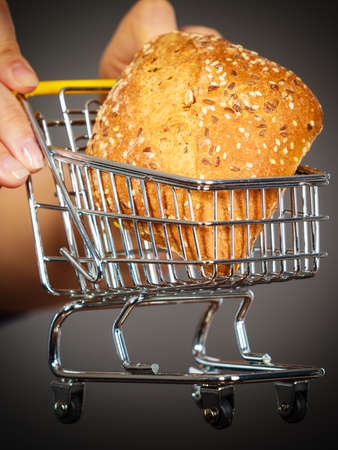 Buying gluten food products concept. Woman hand holding shopping cart trolley with small piece of...