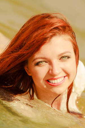 Summer fun, recreation outside concept. Redhead adult woman posing in water during summertime, having great time.の写真素材
