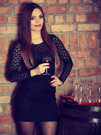 Elegant beauty lady long hair full make up wearing black dress tasting wine in rural cottage interior cellerの写真素材