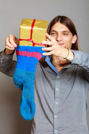 Holiday, xmas winter time season. Stylish guy putting wrapped gift in knitted christmas sockの写真素材