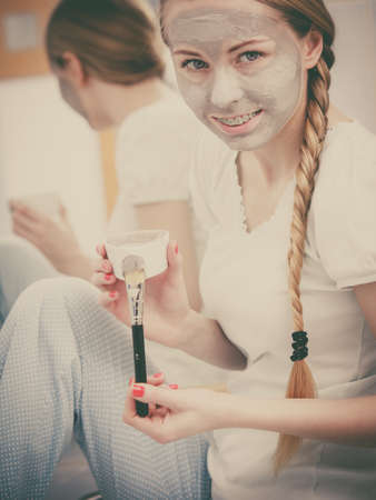 Facial dry skin and body care, complexion treatment at home concept. Happy young woman having grey mud mask on her face showing bowl with dirty brush.の写真素材